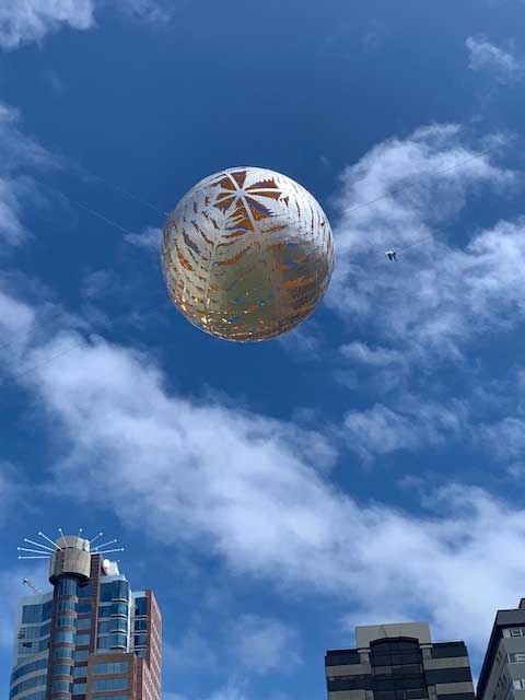 A silver sphere sculpture suspended against a blue sky in central Wellington